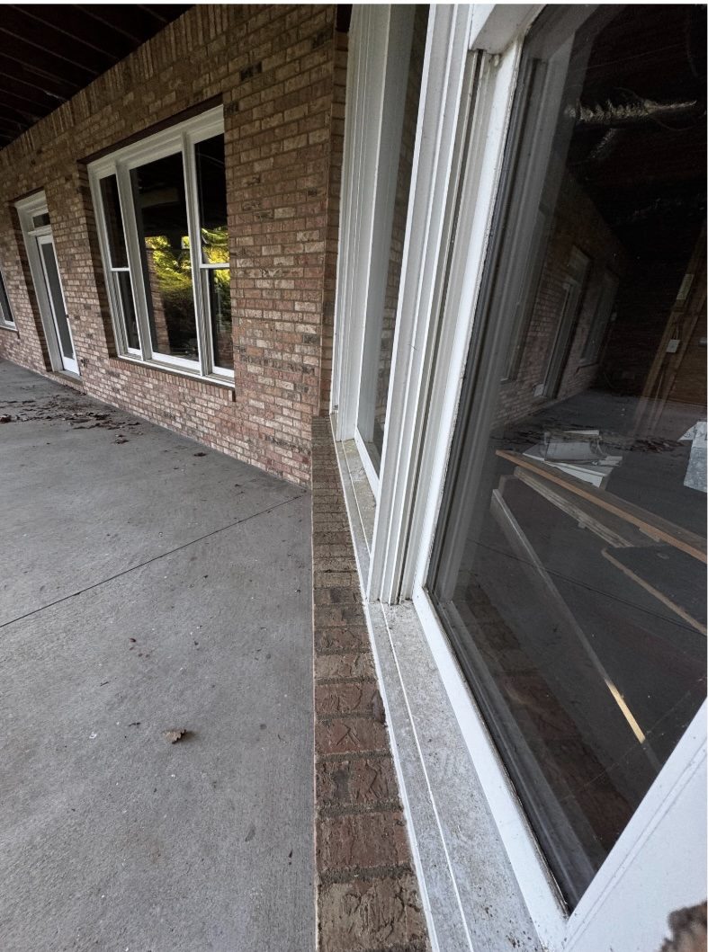 Dirty brick wall, white window trim and concrete walkway along a covered porch in the Summit Top neighborhood on Sweat Mountain, East Cobb, before soft washing