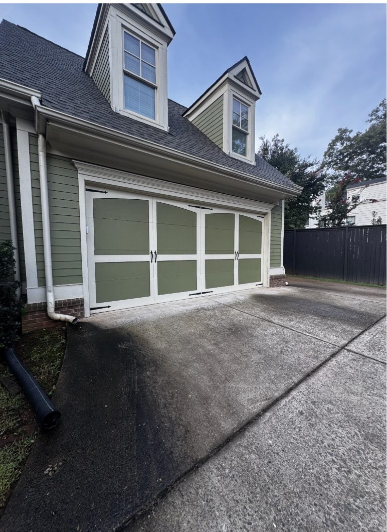 Concrete garage apron stained black and green with algae beside a green sided home near Marietta Square, before pressure washing