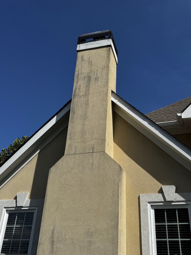 Tan stucco chimney and gable wall streaked with dark gray algae and mildew before soft washing